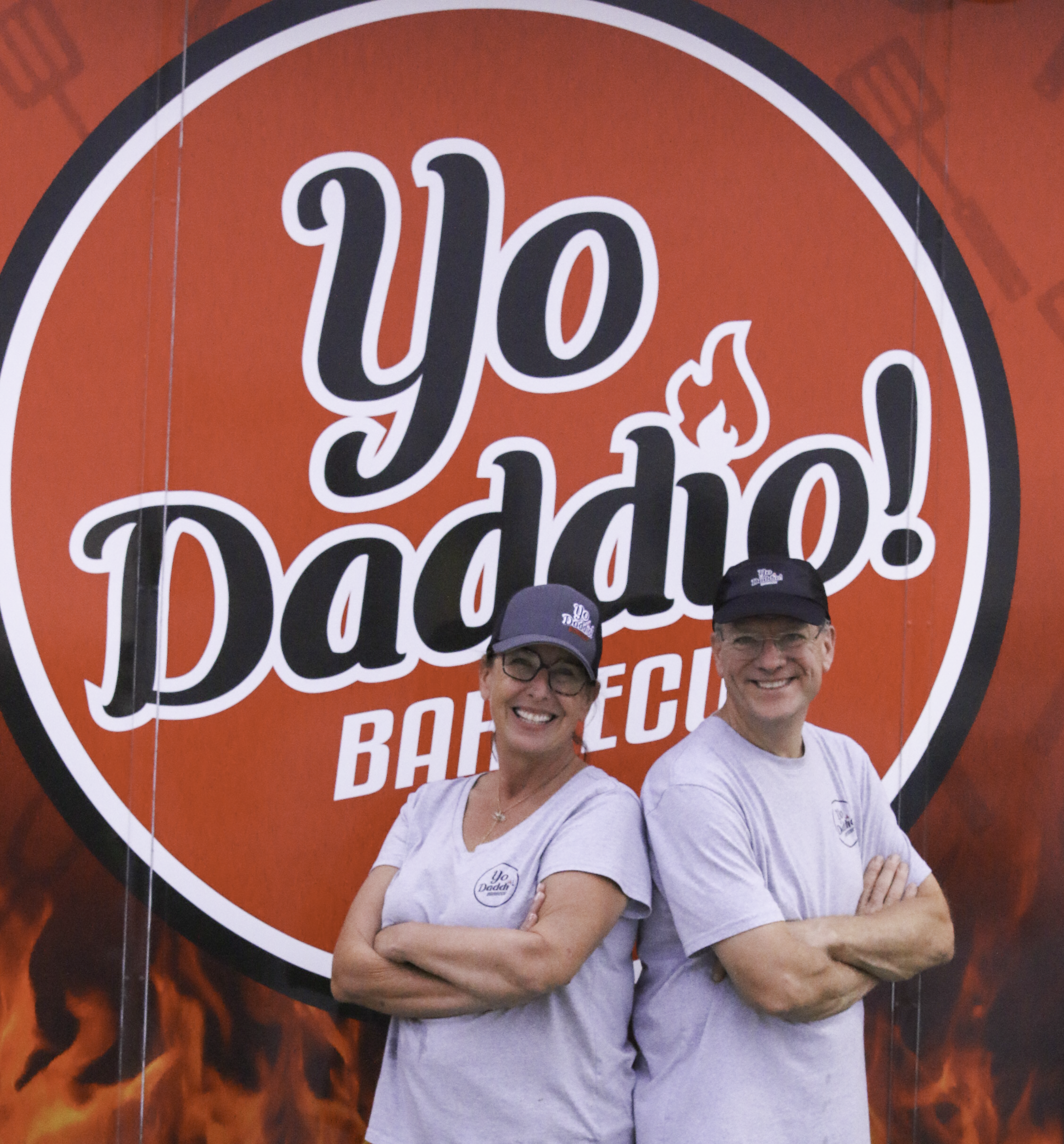 A man and woman standing back to back with arms crossed in front of the You Daddio! Barbecue Food Truck